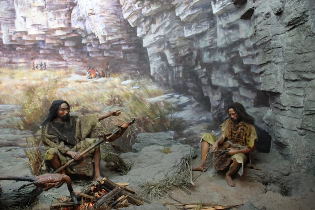 Prehistoric humans cooking meat near a cave fire